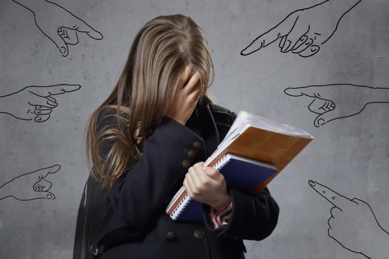 Photo d'une jeune fille qui tient des cahiers d'école et se tient la tête en signe de mal-être à cause du harcèlement scolaire qu'elle subit